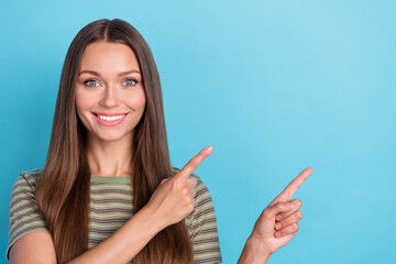 Wall Mural - Photo of optimistic adorable cute girl with long hairstyle wear striped t-shirt directing empty space isolated on blue color background