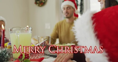 Sticker - Animation of merry christmas text over happy caucasian family in santa hats saying grace at dinner