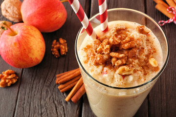 Wall Mural - apple pie smoothie close up in a glass with walnuts and cinnamon. table scene on a rustic dark wood 