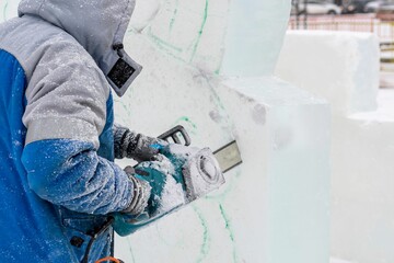 Wall Mural - Sculptor artist using electric saw cuts out New Year's ice figure according to finished sketch.