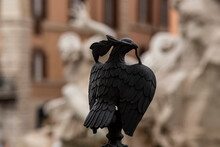 Wrought Iron Peace Dove On The Gate Of A Church, In The Background, Out Of Focus, The Fountain Of The 4 Rivers In Piazza Navona In Rome.
