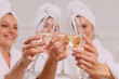 © MZaitsev - A group of women spend leisure time. Young attractive females in bathrobes drink champagne and chat merrily.