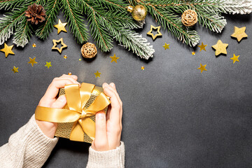 Wall Mural - Boy holding golden gift box with bow on dark background with traditional Christmas and New Year decorations.