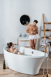 sexy man in underpants lighting cigarette near girlfriend relaxing in bathtub with glass of champagne.