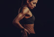 Strong sporty woman doing hand massege to relax the tension in low back and sacrum in sport bra top on empty copy space black studio background. Sports exercises injury. Back view.