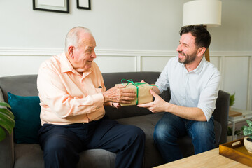 Wall Mural - Cheerful senior father receiving a birthday gift from his smiling son