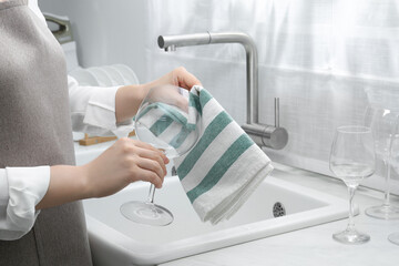 Poster - Woman wiping glass with towel near sink in kitchen, closeup