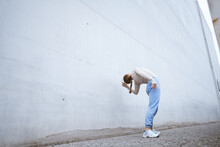 Girl In A Blue Pants Stretching And Dancing Against Grey Wall