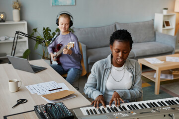 High angle portrait of two young women playing musical instruments at home and recording song together, copy space