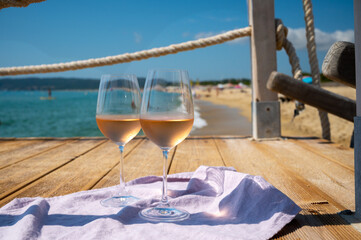 Glasses of cold rose wine from Provence served outdoor on wooden yacht pier with view on blue water and white sandy beach Plage de Pampelonne near Saint-Tropez, France