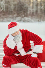 Wall Mural - Vertical portrait of traditional santa Claus sitting on bench outdoors and thinking