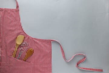 Poster - Red striped apron with kitchen tools on light grey background, top view. Space for text