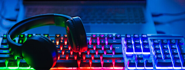 Wall Mural - Pro gaming illuminated desk, headset, keyboard, computer neon lights. Cyber sport equipment laying on desktop, ready for online video gaming.Dark shot.Banner,advertisement.