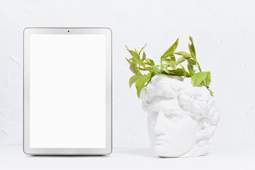 Idea concept with head of white antique statue David, abstract image of his thinking process as young spring green leaves grow of head as thoughts, blank digital silver tablet for text, presentation.