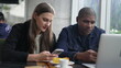An interracial couple looking at cellphones seated at coffee shop. Diverse people smiling using smartphone device. Girlfriend with boyfriend at cafe place