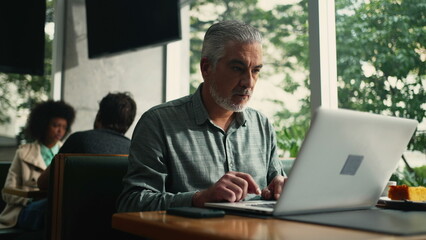 Wall Mural - Older executive opening laptop seated at cafe store working remotely. Middle aged senior man browsing internet online with computer at coffee shop