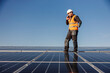 © dusanpetkovic1 - The worker is standing on the rooftop covered with solar panels and talking on the phone.