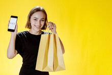 Cheerful Brunette Woman In Black T-shirt Holding Shopping Packages And Phone With Sale Sign