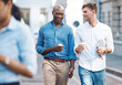 © Charlize D/peopleimages.com - Men, walk and street with takeaway coffee while talk, smile and relax at lunch break. Black man, colleague and diversity in city at tea time, walking to office or workplace in discussion or talking