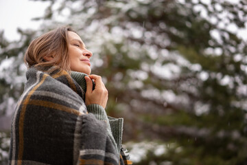 Young adult relaxed woman standing in a sweater and wrapping herself in a scarf standing enjoing fresh air