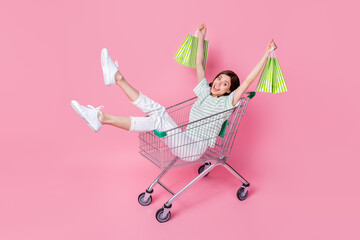 Sticker - Full length photo of cheerful lady sit trolley dressed stylish striped top denim sneakers hold bags isolated on pink color background