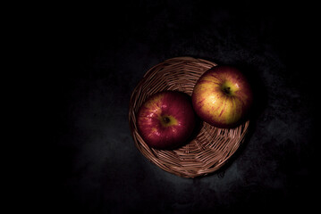 two fresh red apples in a basket On a black background with water droplets, lights are falling with space for text.