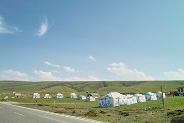 Poster - Scenic view of tents on the green field with hills in the background under blue sky