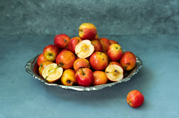 Ripe red small Ranetka apples on a metal plate, on a gray or blue background.. High quality photo