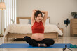 © Apiwan - Happy Asian pregnant woman in sportswear sitting on yoga mat stretching warm up and exercise from looking online class by smartphone in the room at home.
