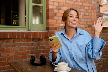 Wall Mural - White young woman using mobile phone while resting in cafe outdoors