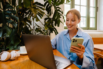 Poster - Young white businesswoman using laptop while sitting by table in cafe