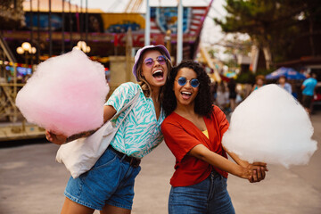 Young multiracial women eating cotton candy in attraction park