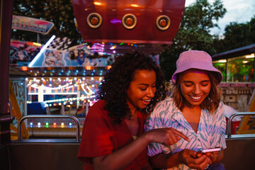 Wall Mural - Young multiracial women using cellphone while riding on ferris wheel