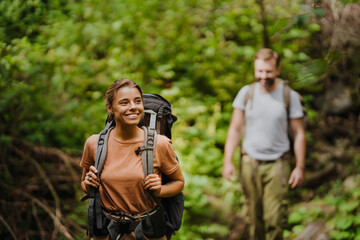 Wall Mural - White young couple with backpacks hiking in green forest