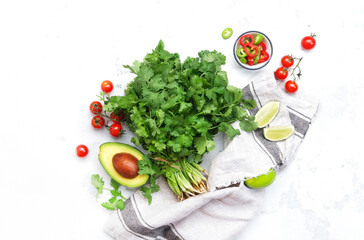 Wall Mural - Fresh cilantro or coriander, chili and jalapeno peppers, avocado, lime and cherry tomatoes - ingredients for Mexican spicy cuisine. White kitchen table background, top view