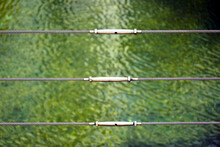 Stainless Steel Turnbuckle And Twisted Wire Cable Safety Railing Balustrade Along Shallow Pool Edge With Green Water And Reflections. Deep Green Algae In The Water. Safety And Security Concept.
