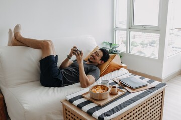 Lazy happy asian man playing mobile game while he should have work from home.