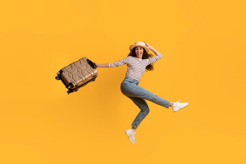 Wall Mural - Cheerful Young Female Traveller Jumping With Suitcase In Hands Over Yellow Background