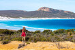 a beautiful long-haired girl stands on a hill overlooking a wonderful paradise beach with turquoise water and white sand. The famous lucky bay beach near esperance in western australia, cape le grand