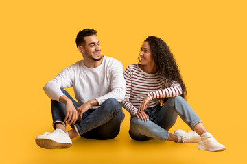 Wall Mural - Portrait of beautiful young middle eastern couple sitting together over yellow background