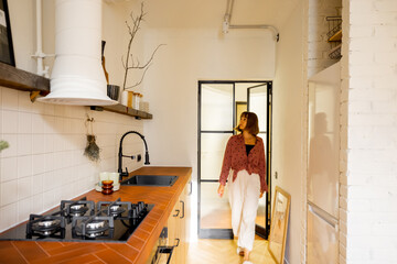 Stylish kitchen interior of modern apartment with motion blurred female person walking inside. Interior made in white and beige tones with tiled table top and glass door