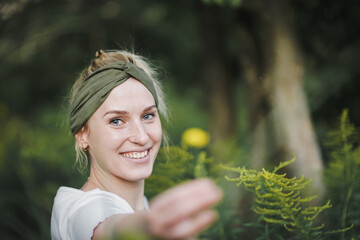 Wall Mural - 
happy alternative & spiritual looking hipster woman holding yellow flower into the cam like a present or gift outside in a park with green nature background 
