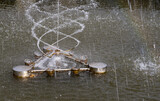 Fototapeta Tęcza - Fontanna w parkowym stawie , wystrzeliwująca spirale strumienie wody . Widoczna  miniaturowa tęcza .