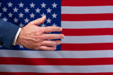 Open Hand Waiting To Be Shaken With The United States Flag In The Background. Doing Business With Americans. Peace And Cooperation Agreements