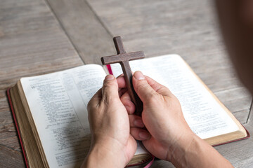 Hand holding religious crucifix cross on top of Holy Bible. Christian faith and devotion concept.