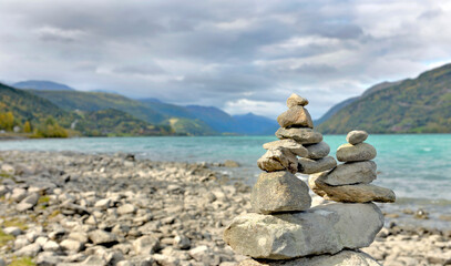 Wall Mural - cairn at the water's edge on a pebble beach and on mountainous landscape of norway