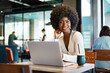 © fotofabrika - Smiling young african woman sitting with laptop in cafe