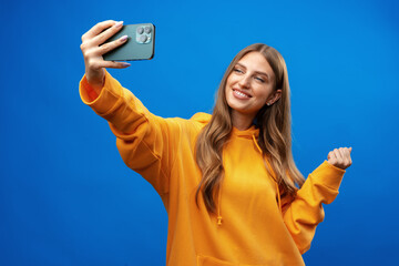 Photo of attractive young woman takes selfie photo on smartphone on blue background