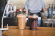 Iced chocolate and iced mocha on table with blurred back view of baretta at coffee shop
