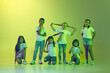 Group of children, little girls and boys in sportive casual style clothes dancing isolated on green background in yellow neon light.